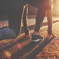 Runner preparing to sprint, crouched on a sunlit road, ready to launch forward in the warm glow of sunrise.